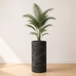 Potted indoor palm plant in tall charcoal grey cylindrical planter with stone texture on light wood floor.